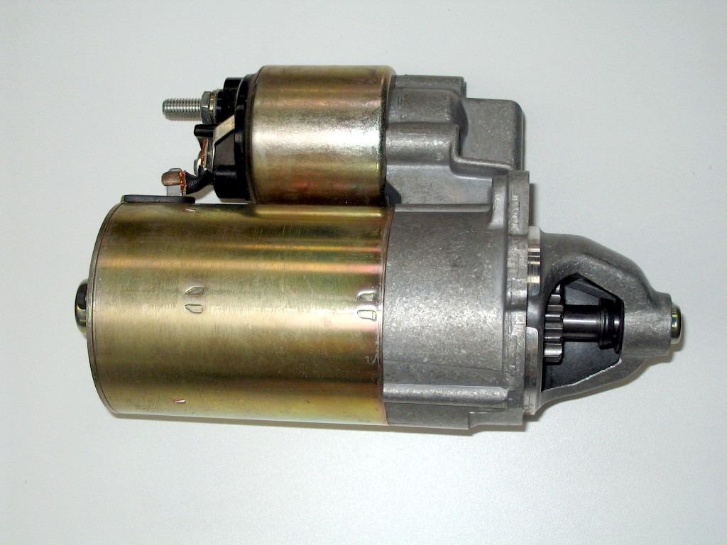 Un motorino d'avviamento con il suo solenoide, appoggiato su un fondo chiaro
